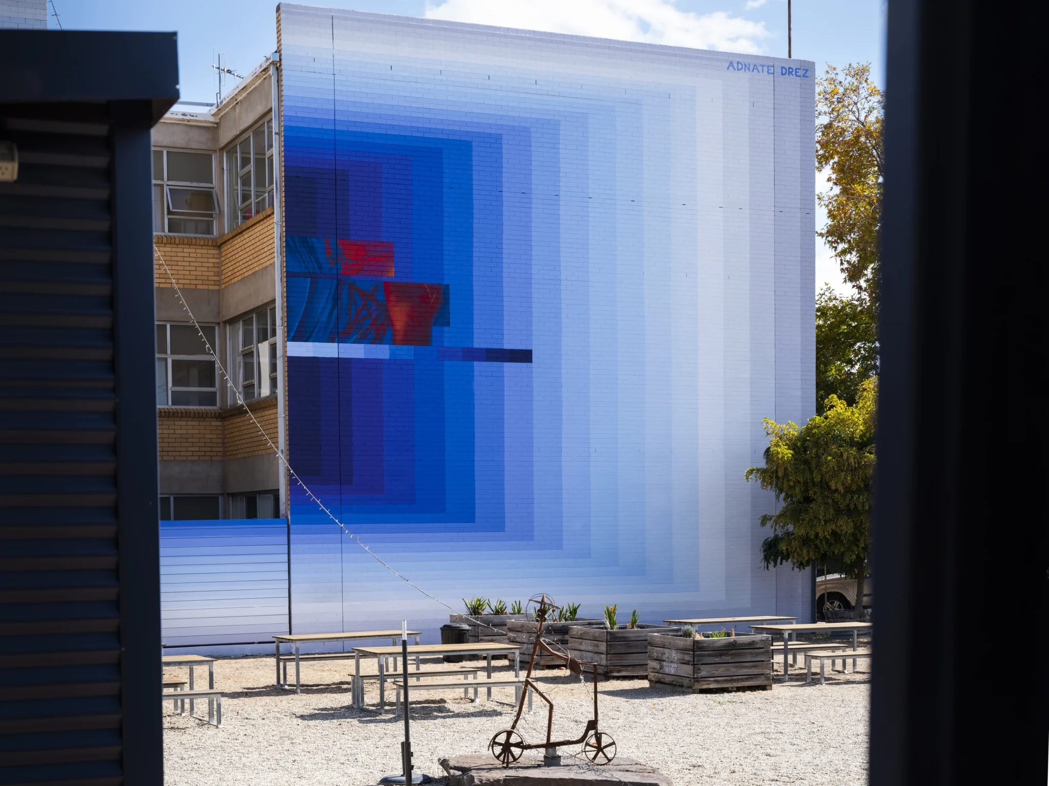 Soft blue and purple hues reflect the surrounding sky, while bordering grey tones echo shifting daylight, together visually connecting the work to its environment and integrating it with nature’s cycles. This artwork was part of the 2025 Benalla Street Art Festival.